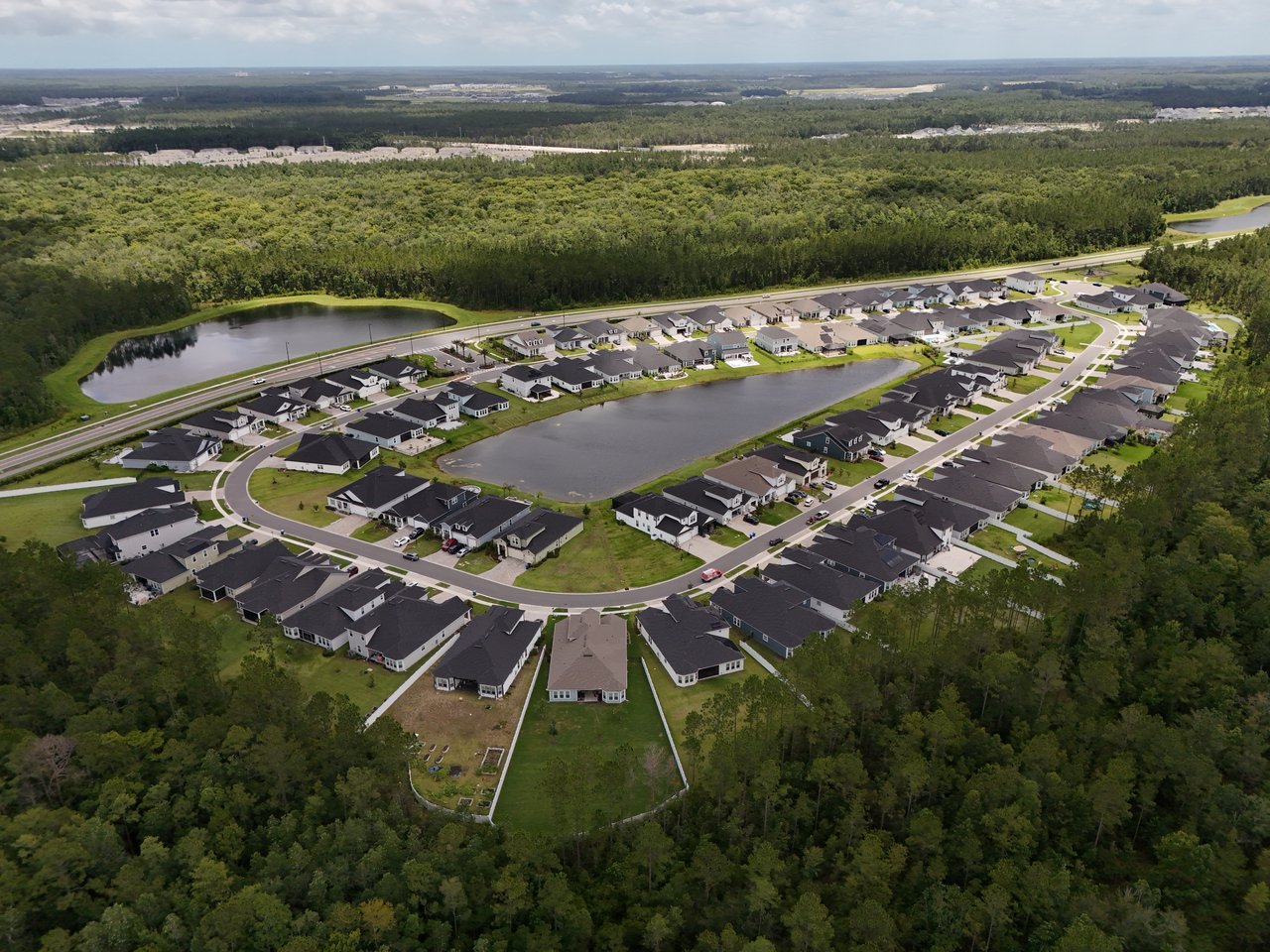 Aerial view of homes around a large pond, with wooded land beyond the neighborhood.
