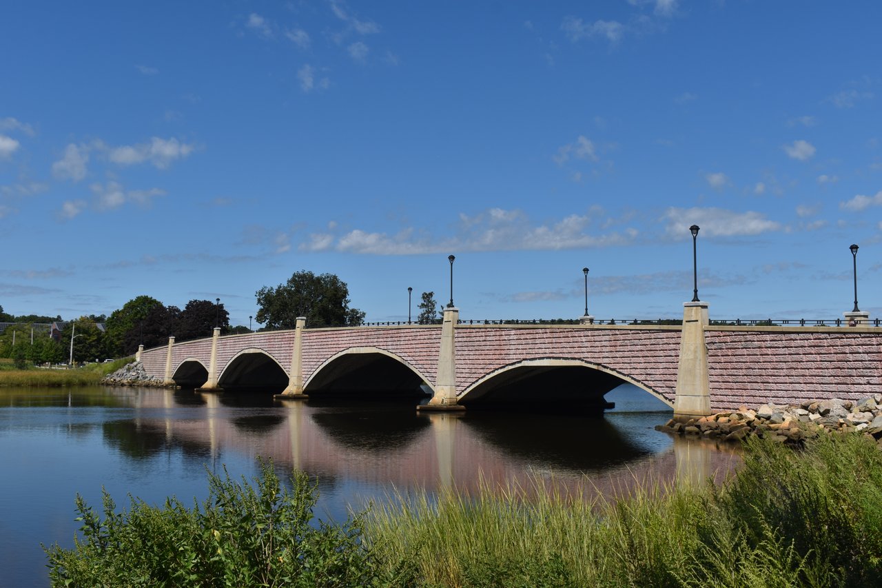 Arched pink brick-and-stone bridge crossing calm water, with lamp posts along its railing.