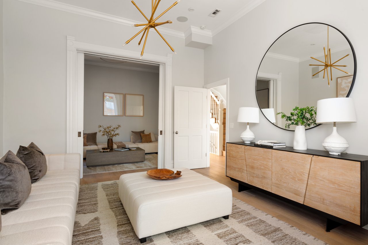 Furnished living room with a white sectional, wood sideboard, round mirror, and gold chandelier.