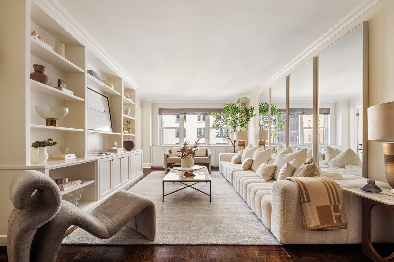 Staged living room with a white sectional, built-in shelves, mirrored panels, and large windows.
