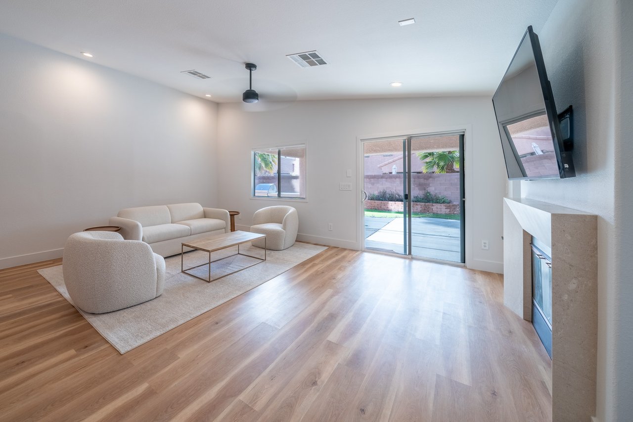 Staged living room with cream seating, light wood floors, and sliding glass doors to a patio.