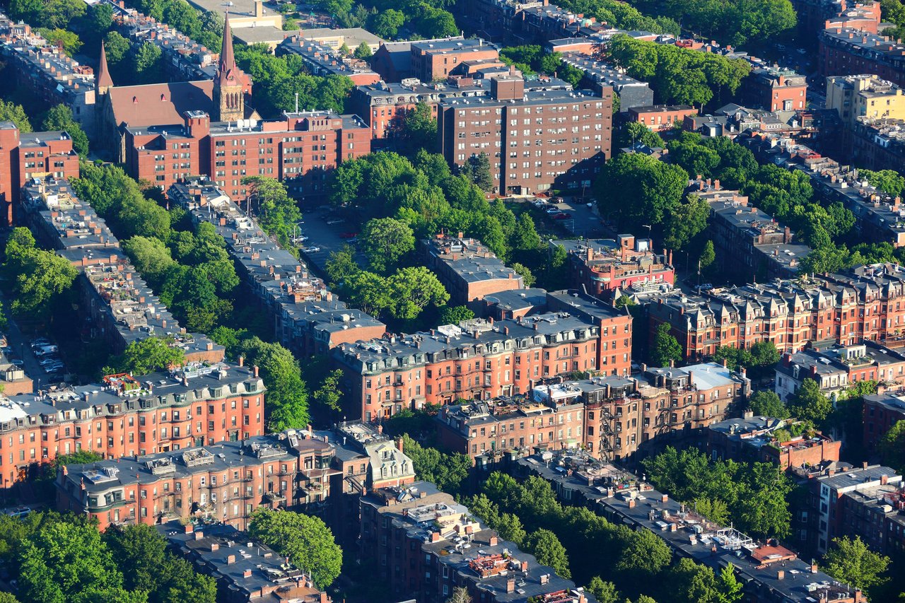 Aerial view of a tree-lined urban neighborhood with red-brick apartment buildings and a church with pointed towers.