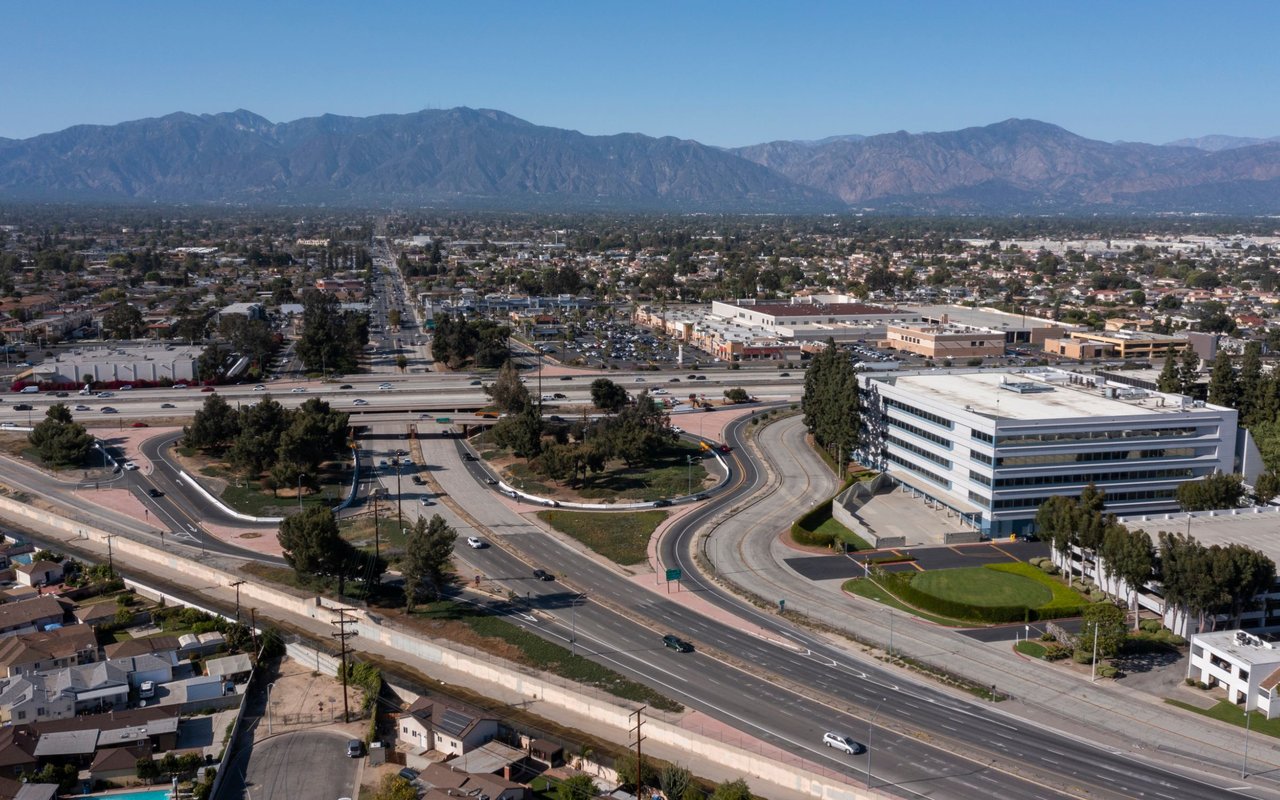 Aerial view of El Monte with freeway ramps, commercial buildings, homes, and mountains beyond.