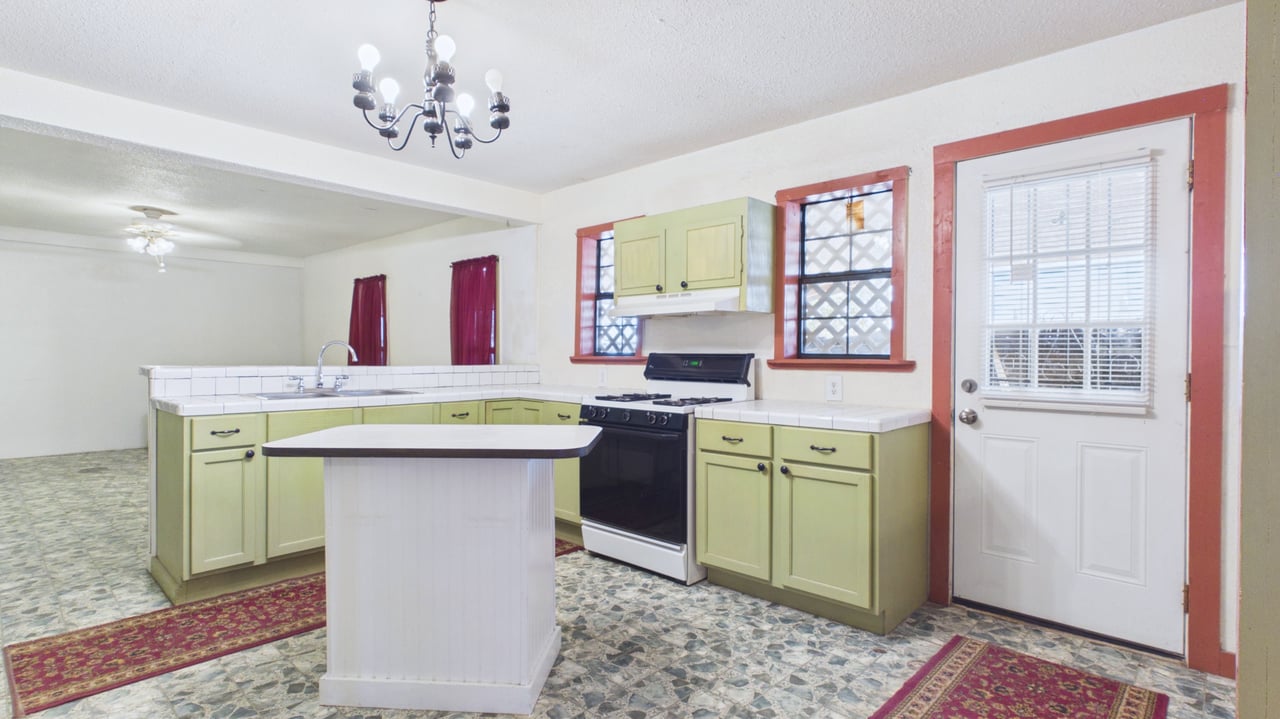 Kitchen with pale green cabinets, central island, gas range, and patterned tile flooring.