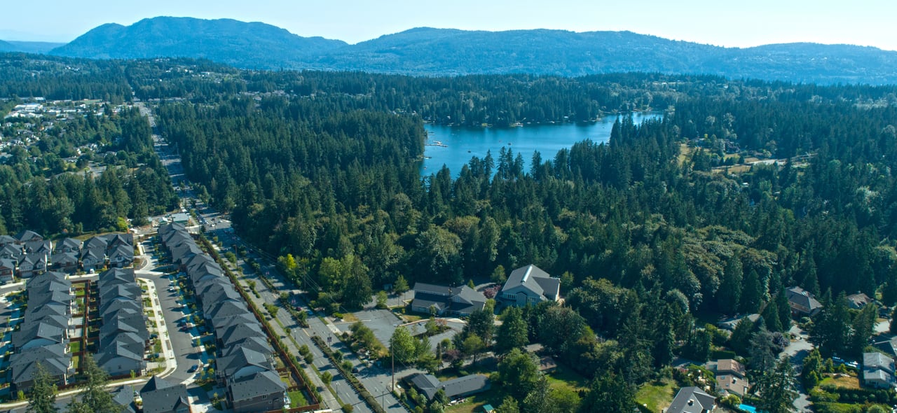 Aerial view of a Redmond neighborhood, with homes, a forested lake, and hills in the distance.