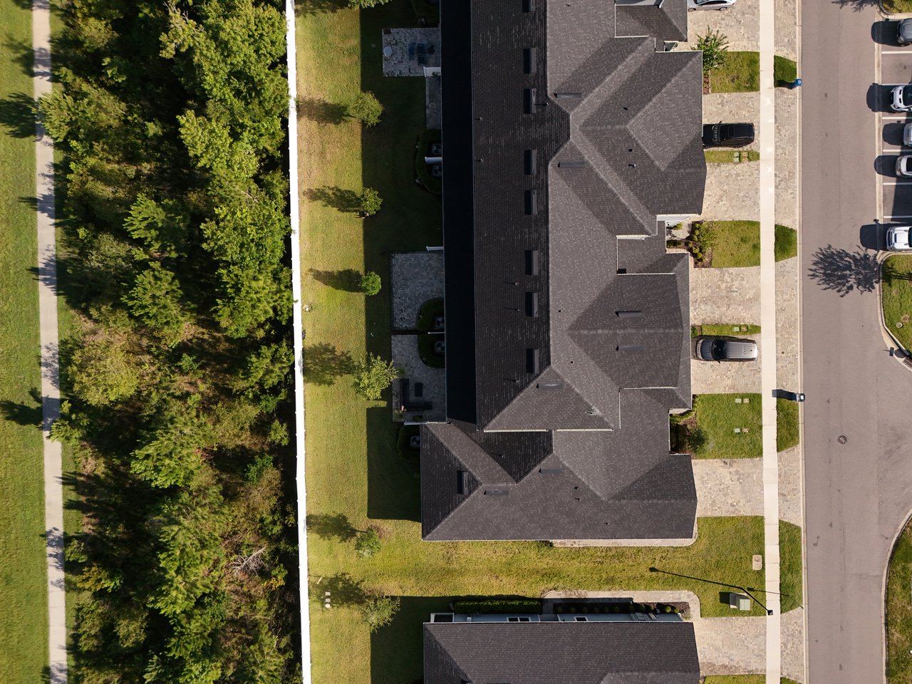 Aerial view of a large home beside a wooded strip, with lawns and neighboring houses.