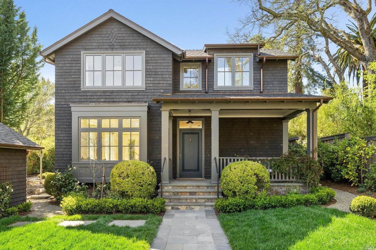 Gray two-story shingle home with a covered porch, stone steps, and landscaped front garden.