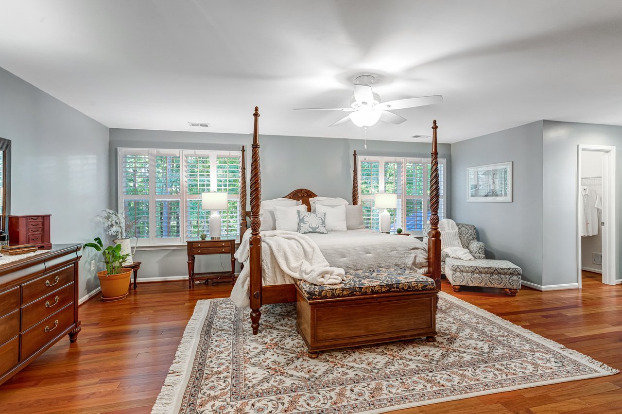 Bedroom with a carved four-poster bed, plantation shutters, and hardwood floors.