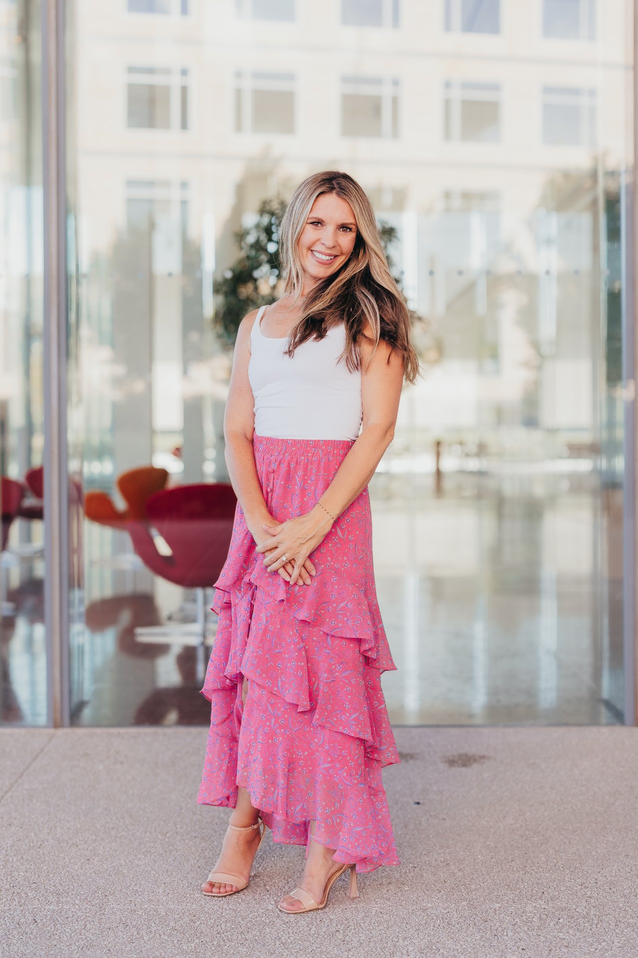 Casey Blancett standing outside a glass-fronted building in a pink floral dress.