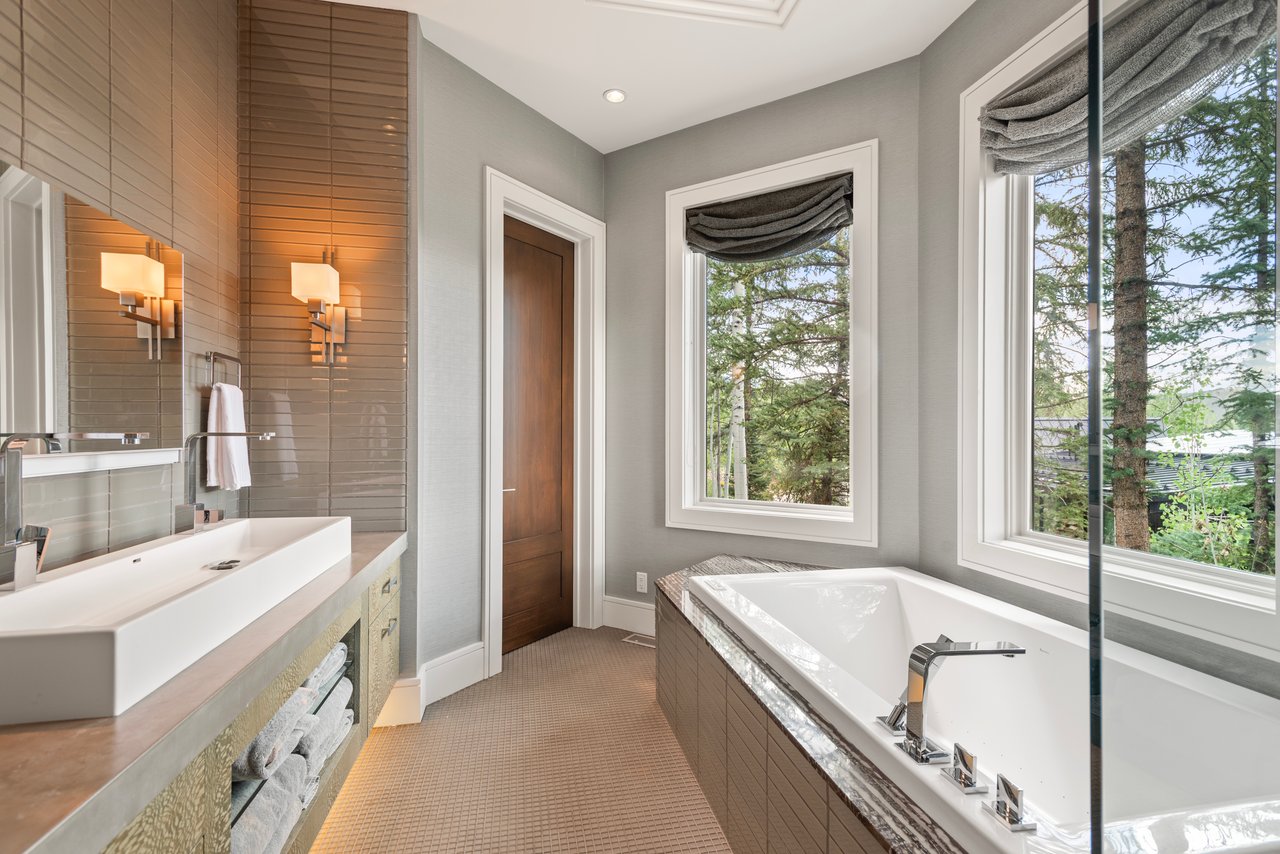 Bathroom with a large soaking tub beside tall windows overlooking evergreen trees.