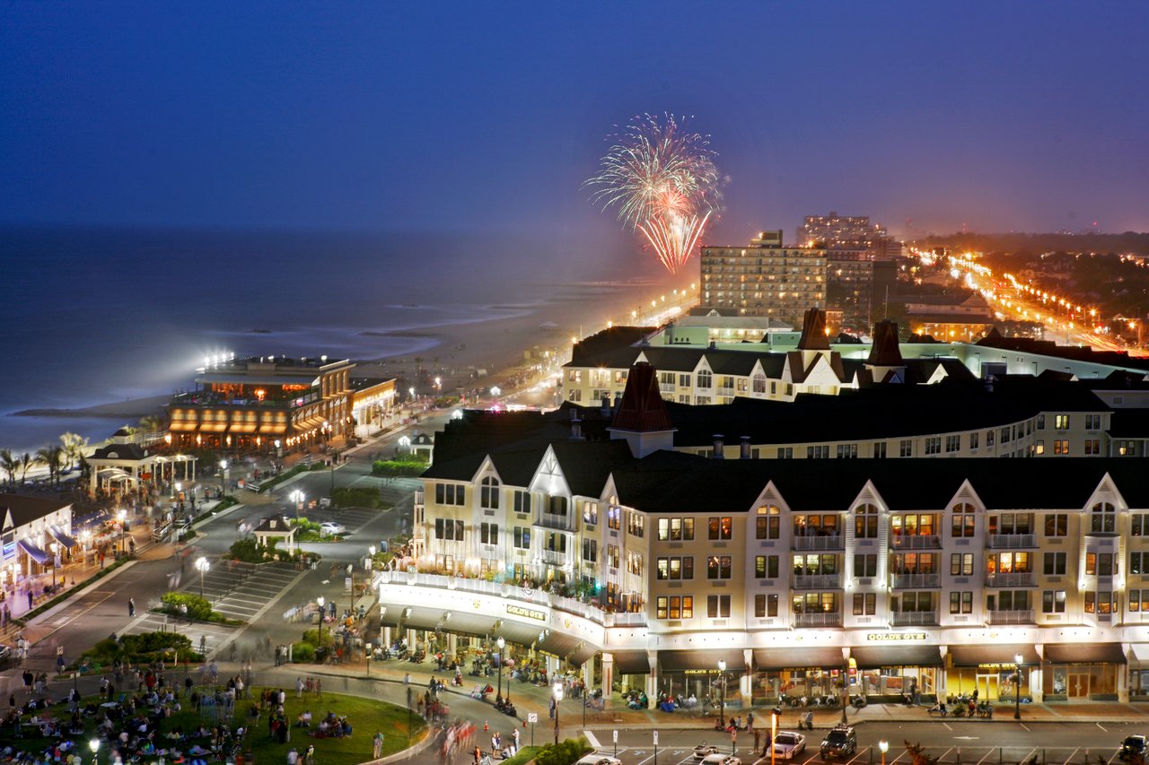 Oceanfront buildings and boardwalk at night, with fireworks over the water.