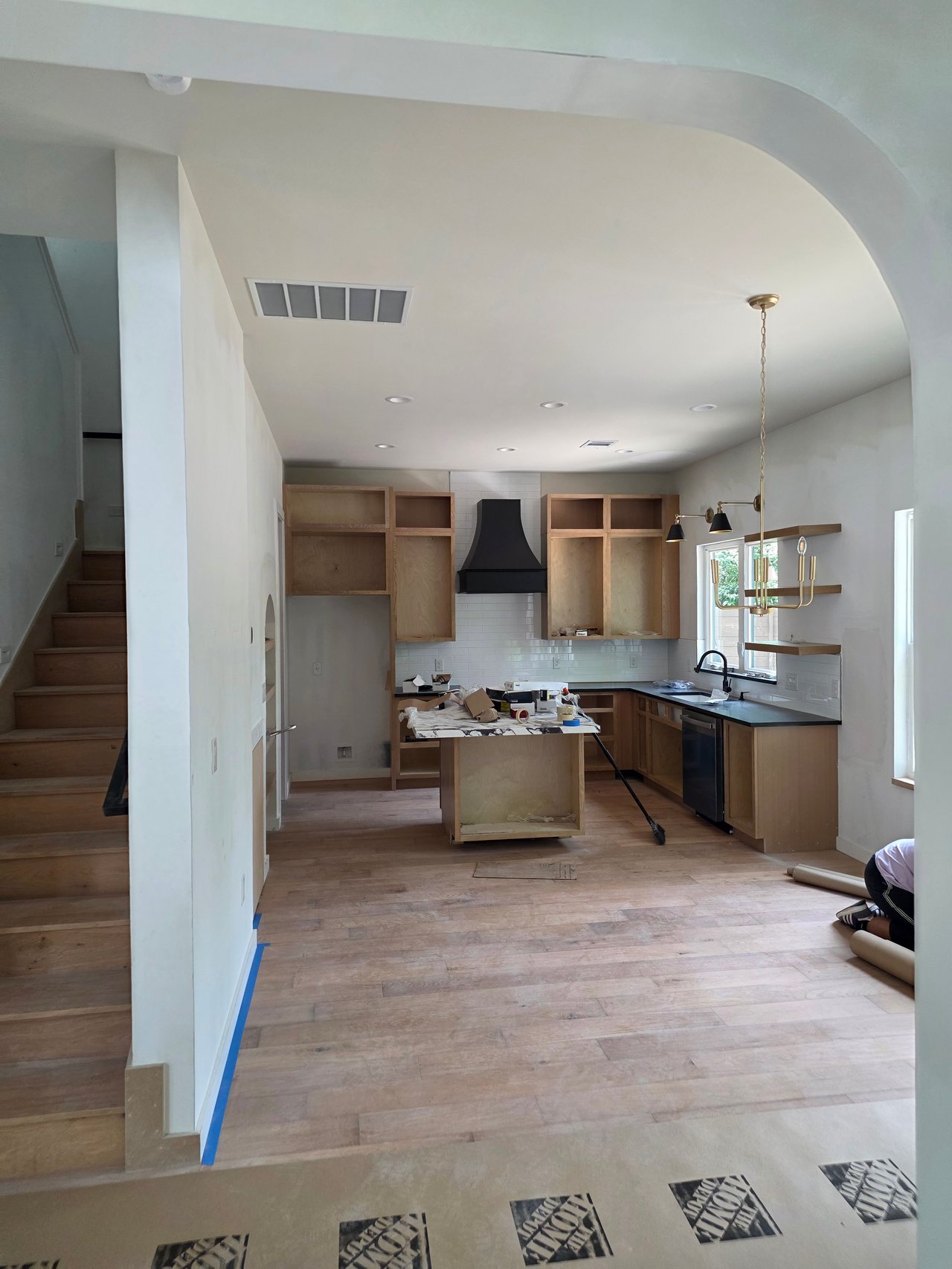 Kitchen under construction with unfinished wood cabinets, a central island, and a staircase along the left wall.