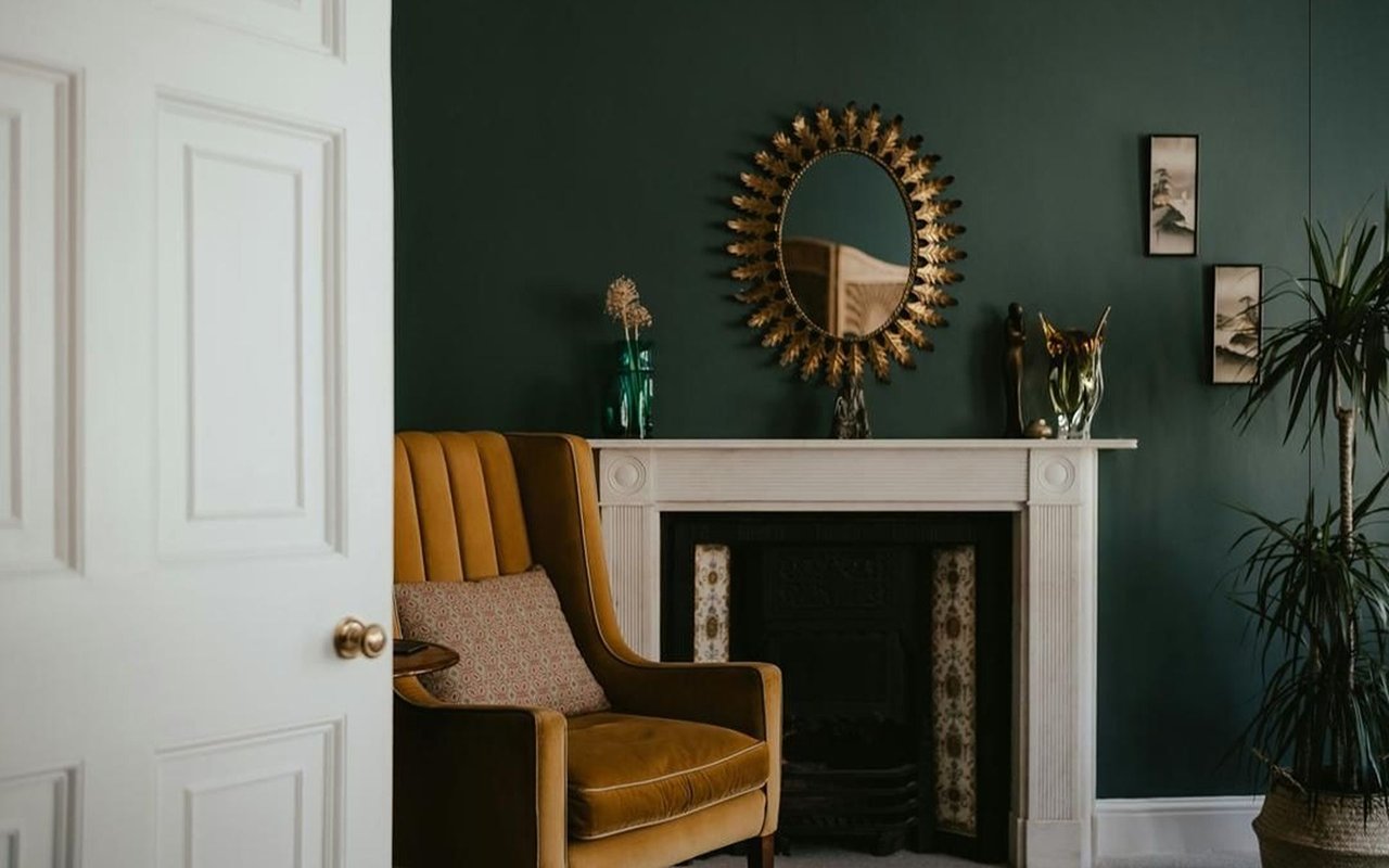Living room with a forest-green wall, white fireplace, and mustard-gold chair