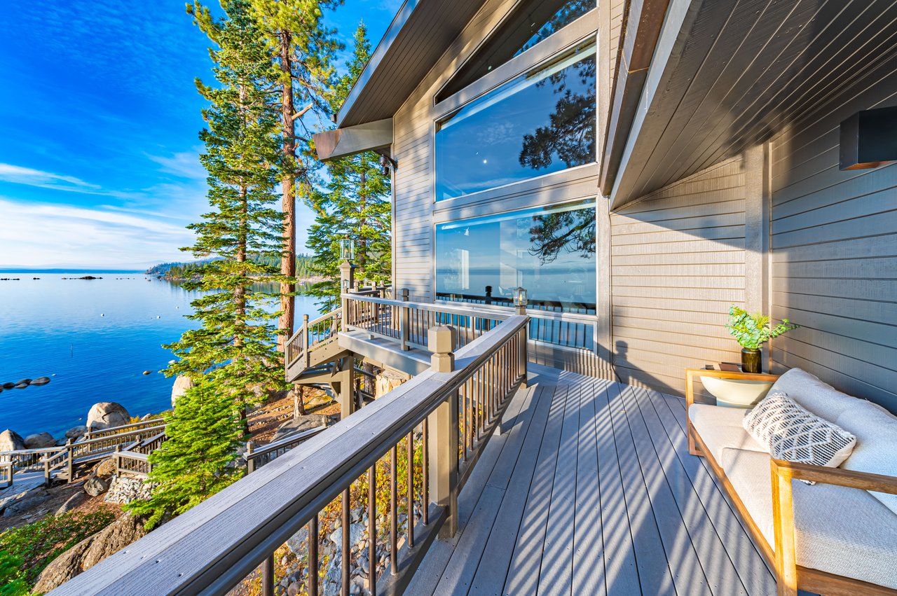 Lakeside deck with outdoor seating, large windows, and views of blue water and pine trees.