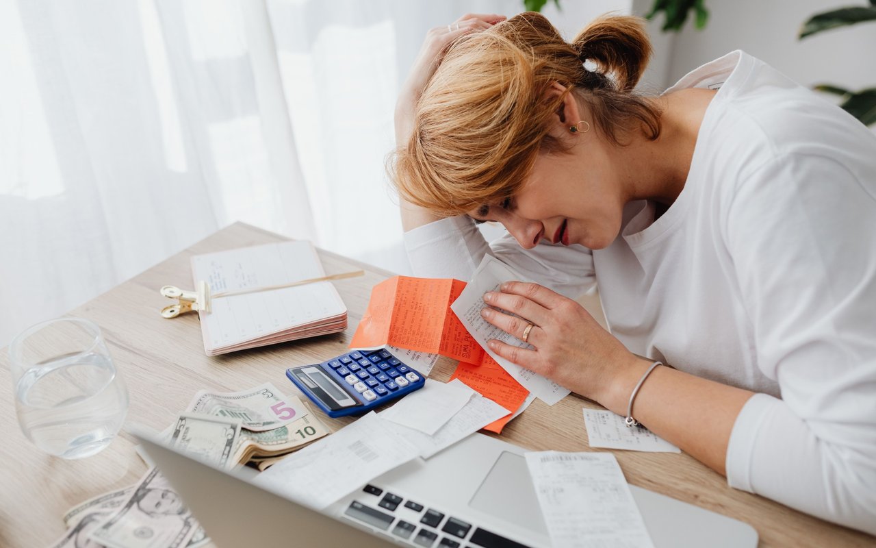 Stressed woman reviewing bills and receipts at a desk with a calculator and cash.