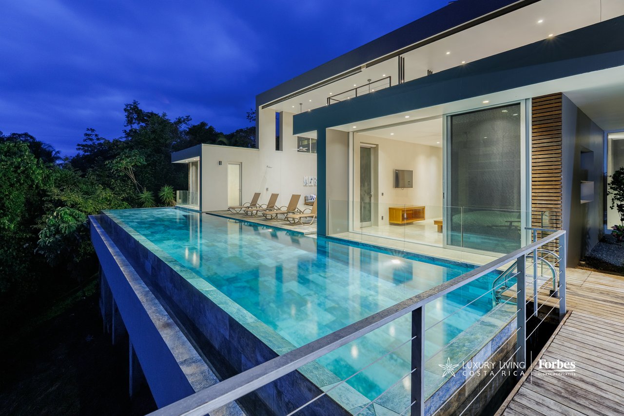 Modern home with an infinity pool and glass-fronted living area at dusk.