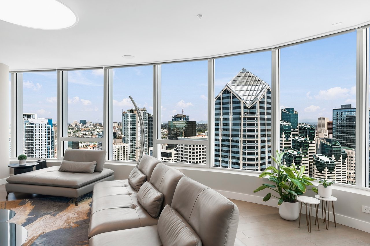 High-rise living room with leather sofas and floor-to-ceiling windows overlooking downtown towers.