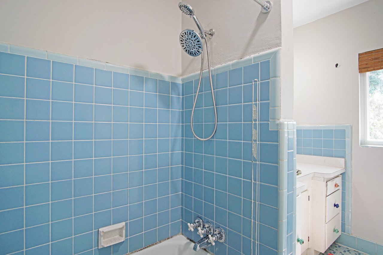 Retro bathroom with blue tiled walls, dual showerheads, and a white tub. A vanity with colorful knobs is partially visible. Bright and clean atmosphere.