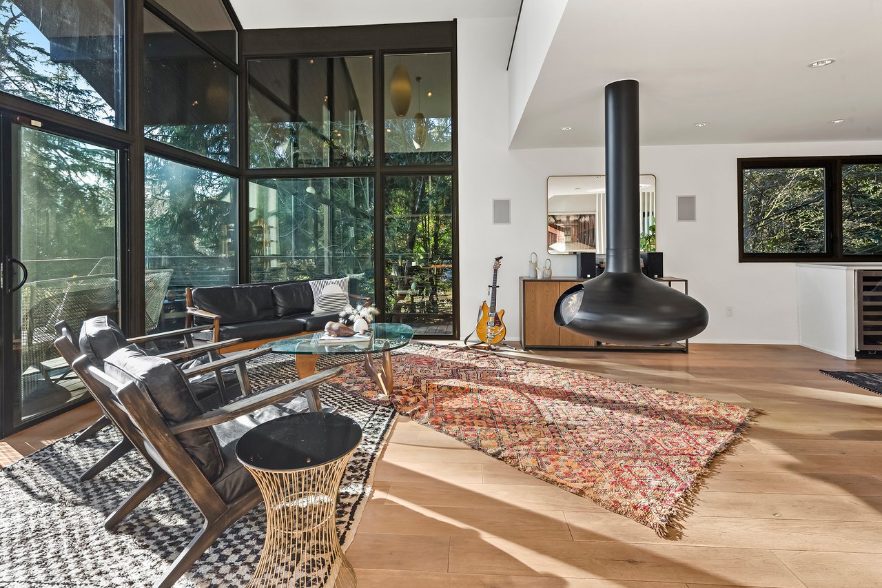 Modern living room with floor-to-ceiling windows, a suspended black fireplace, and colorful patterned rug.