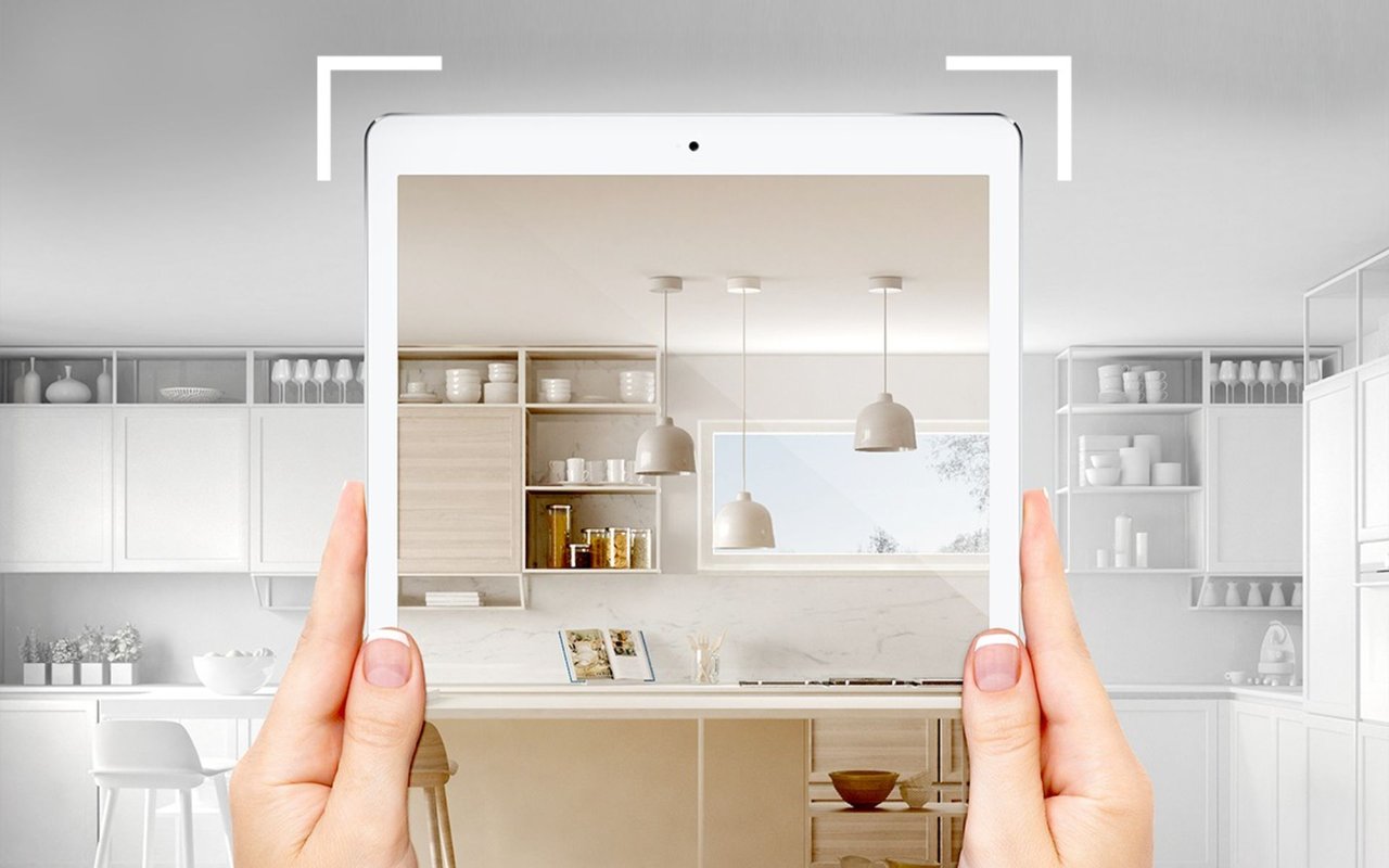 Hands hold a tablet showing a modern kitchen during a virtual home tour.