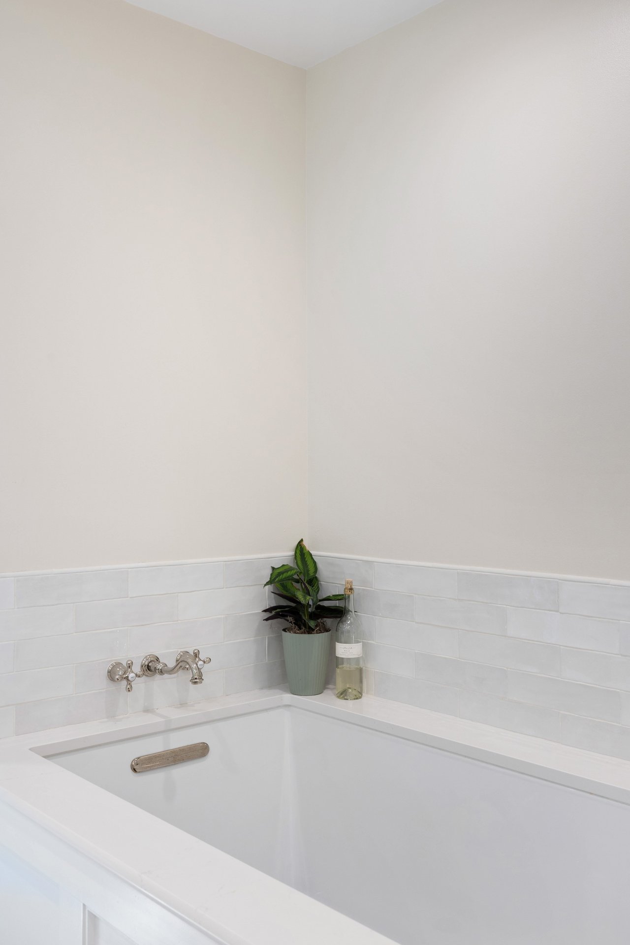 White bathtub with chrome faucet, subway tile surround, and a potted plant in the corner.