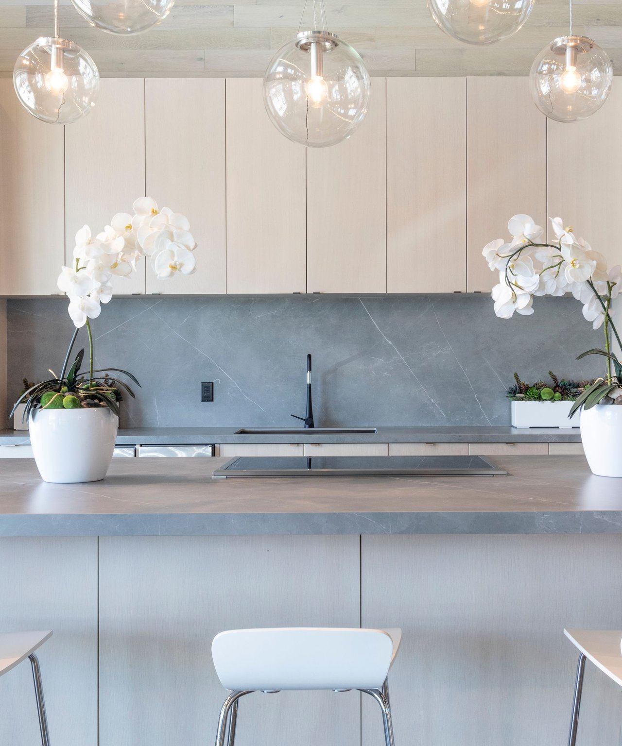 Modern kitchen with a gray stone island, globe pendant lights, and white orchids.