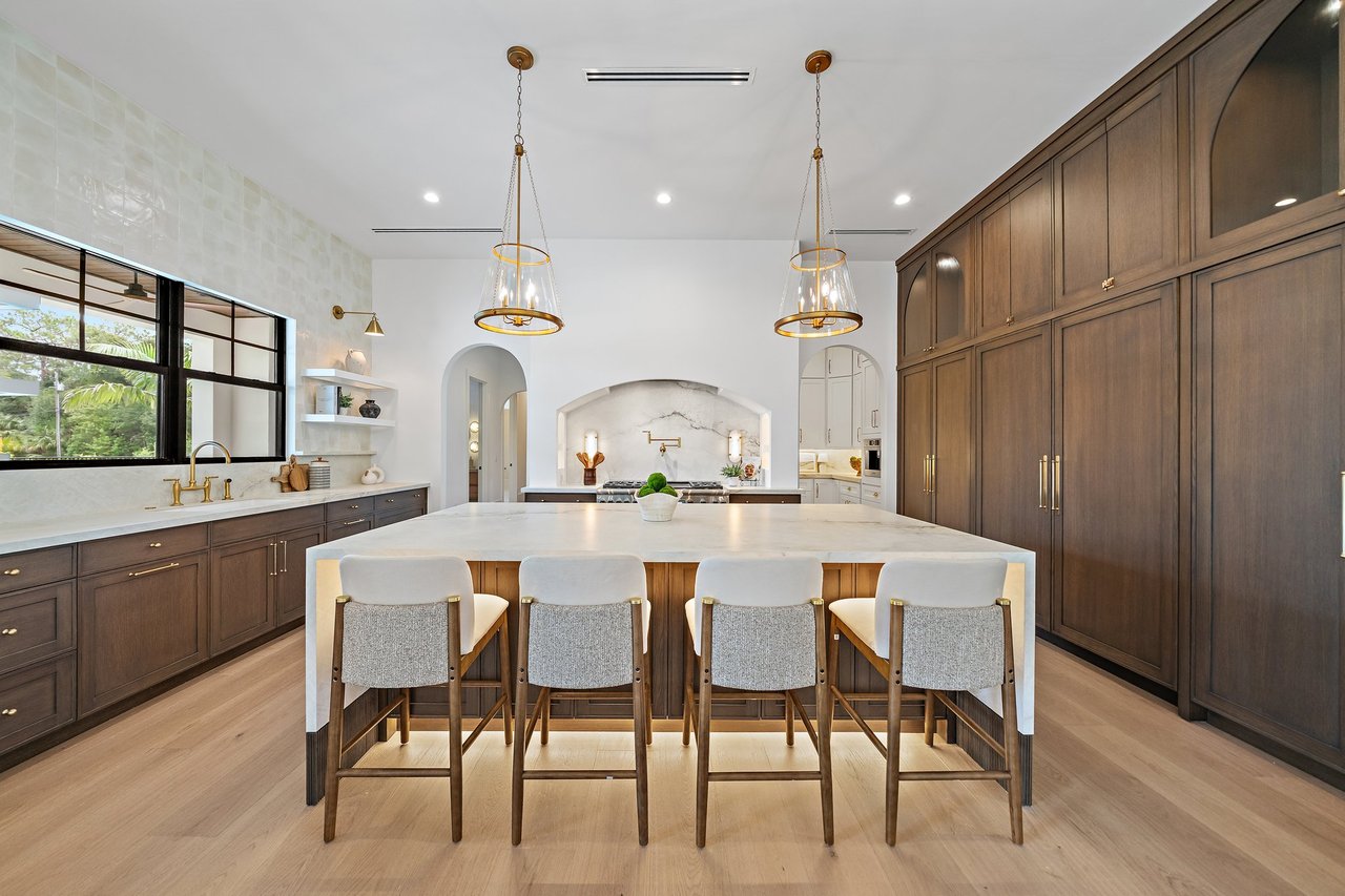 Luxury kitchen with a large island, four bar stools, dark wood cabinetry, and a marble backsplash.
