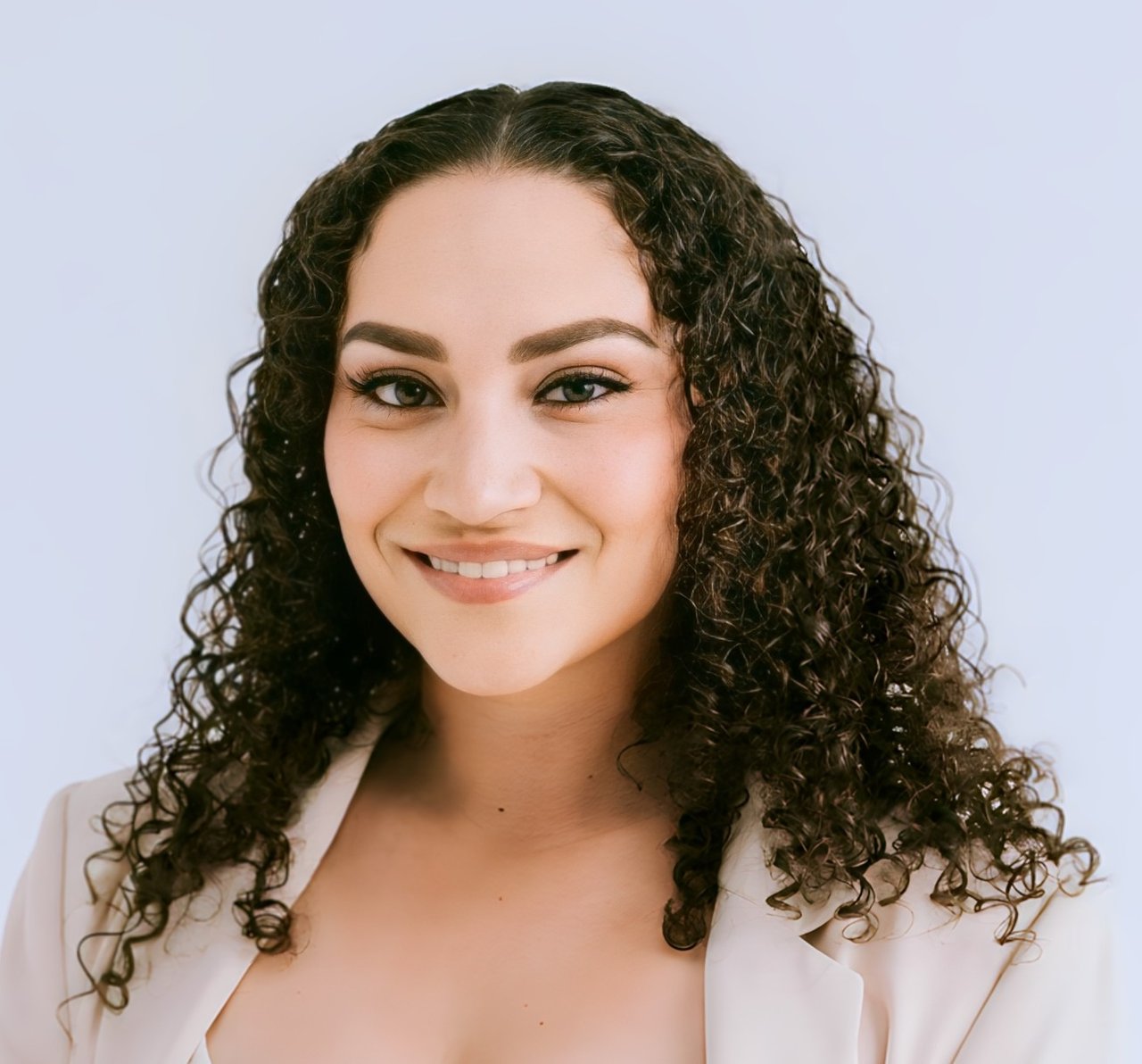Karrissa Gore smiling in a light blazer, with long dark curly hair.
