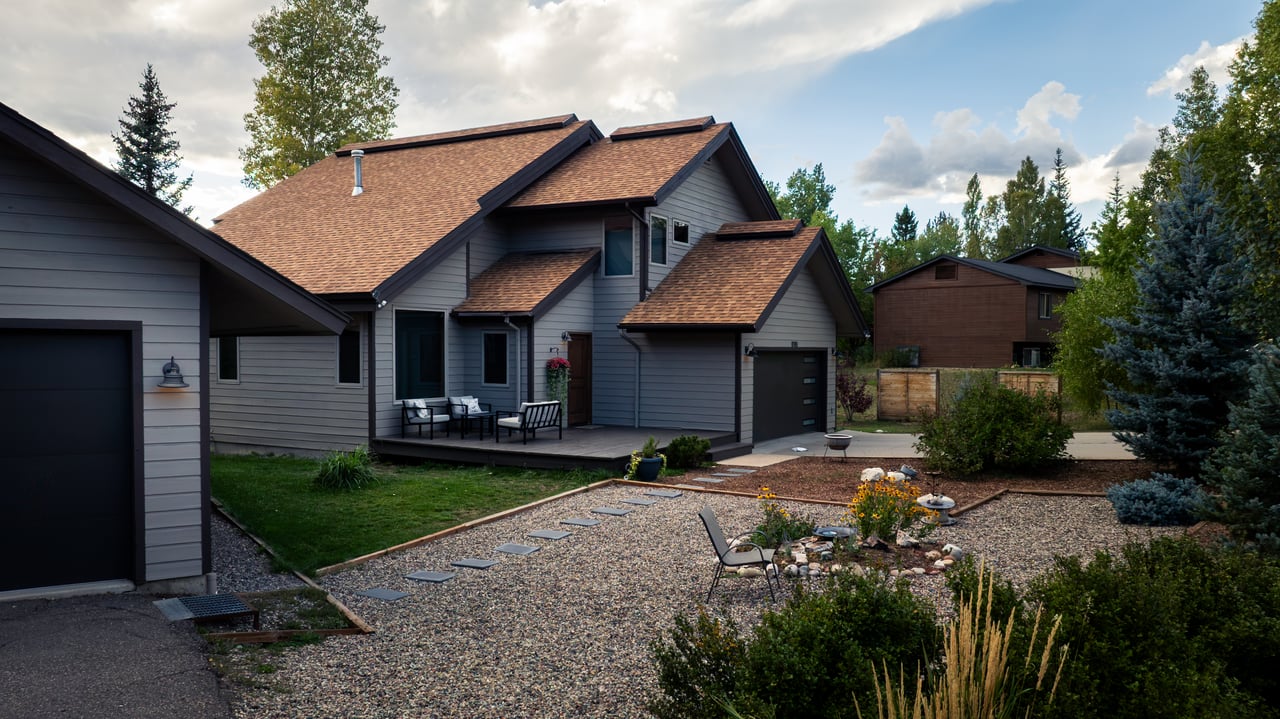 Gray-sided home with a gravel yard, flower beds, stepping stones, and patio seating.