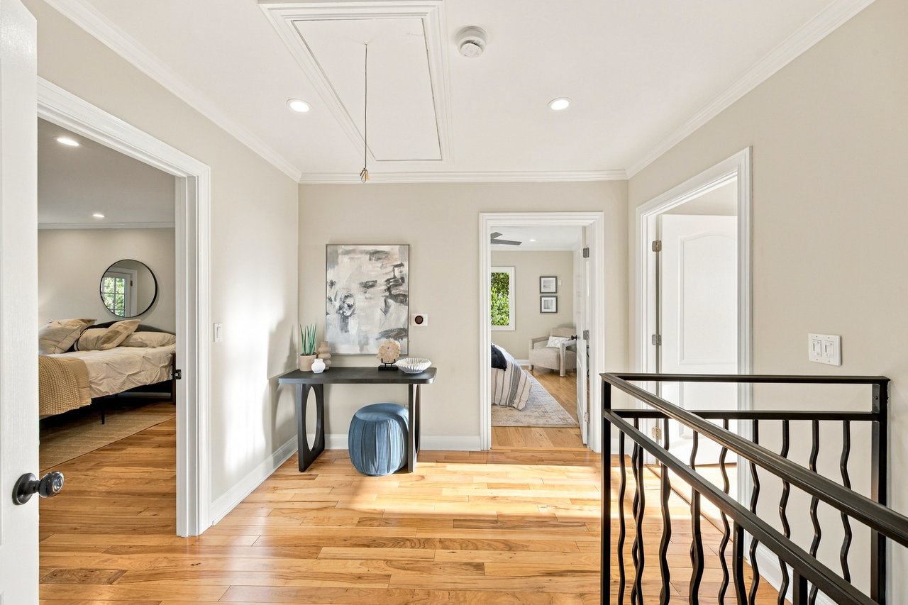 Bright upstairs landing with hardwood floors, a black railing, and doorways to furnished bedrooms.