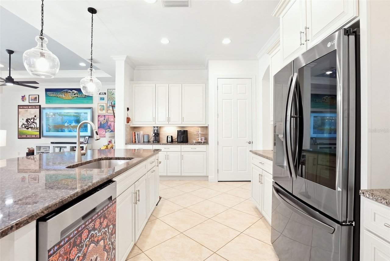 Bright white kitchen with a granite island, stainless steel appliances, and colorful artwork in the adjoining living area.
