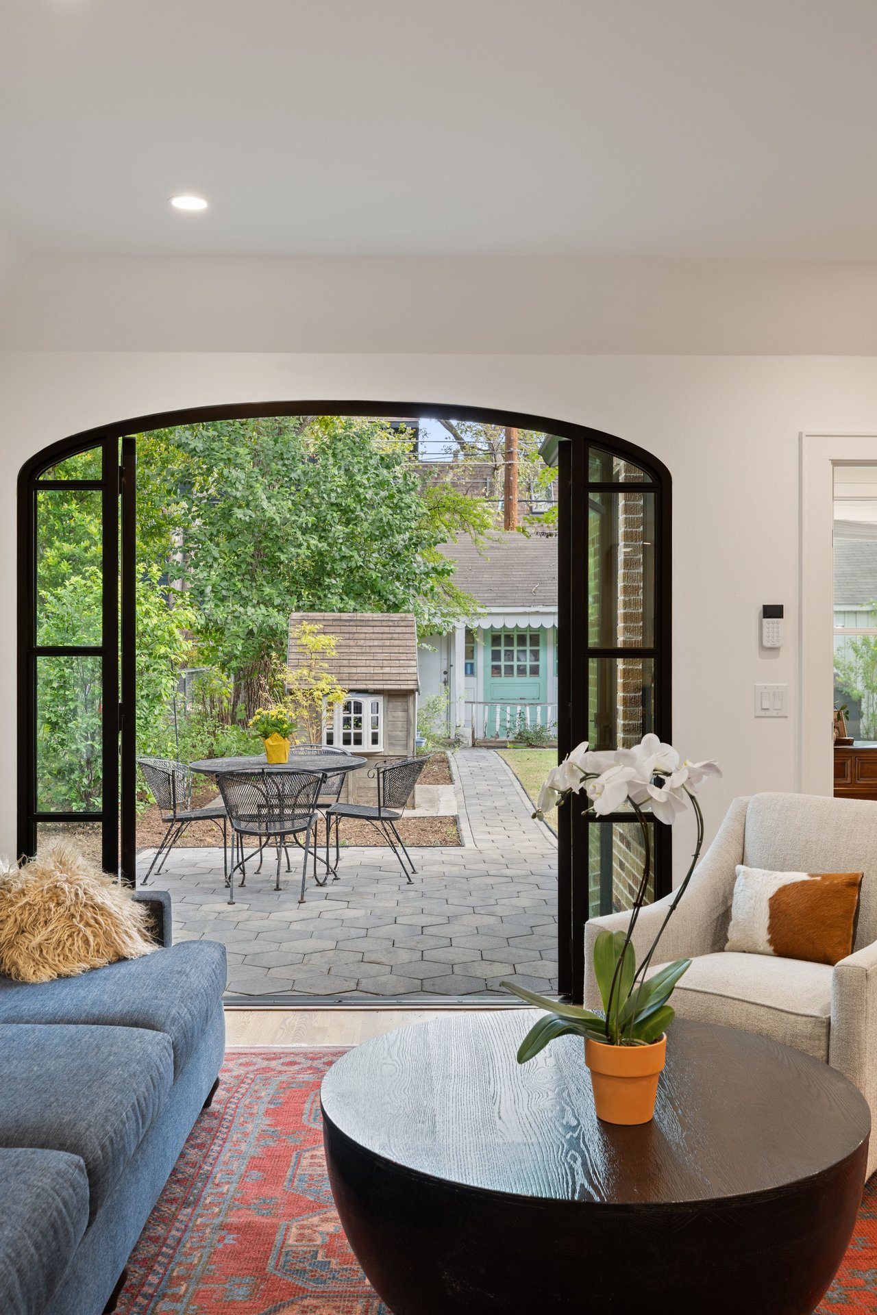 Living room with arched black-framed doors opening onto a leafy patio.