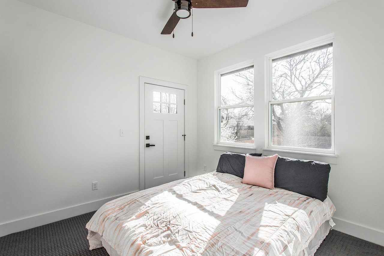 Bedroom with a patterned bedspread, pink pillow, and two large windows.