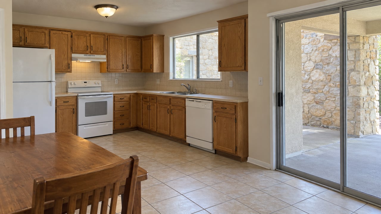 Ranch kitchen with honey oak cabinets, a sink beneath a tall window, and a sliding glass door to a stone patio.