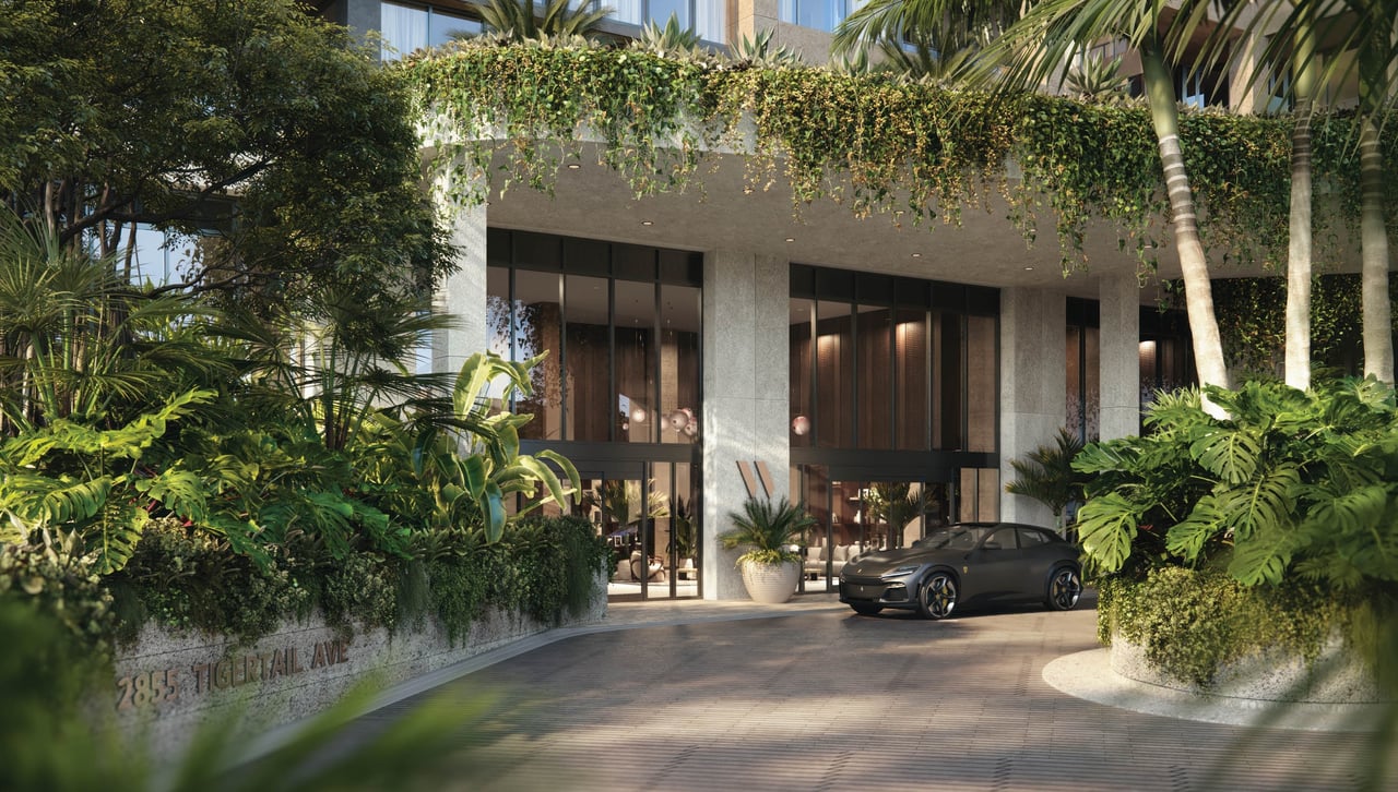The Well’s glass-fronted entrance framed by lush tropical landscaping, with a dark car on the driveway.