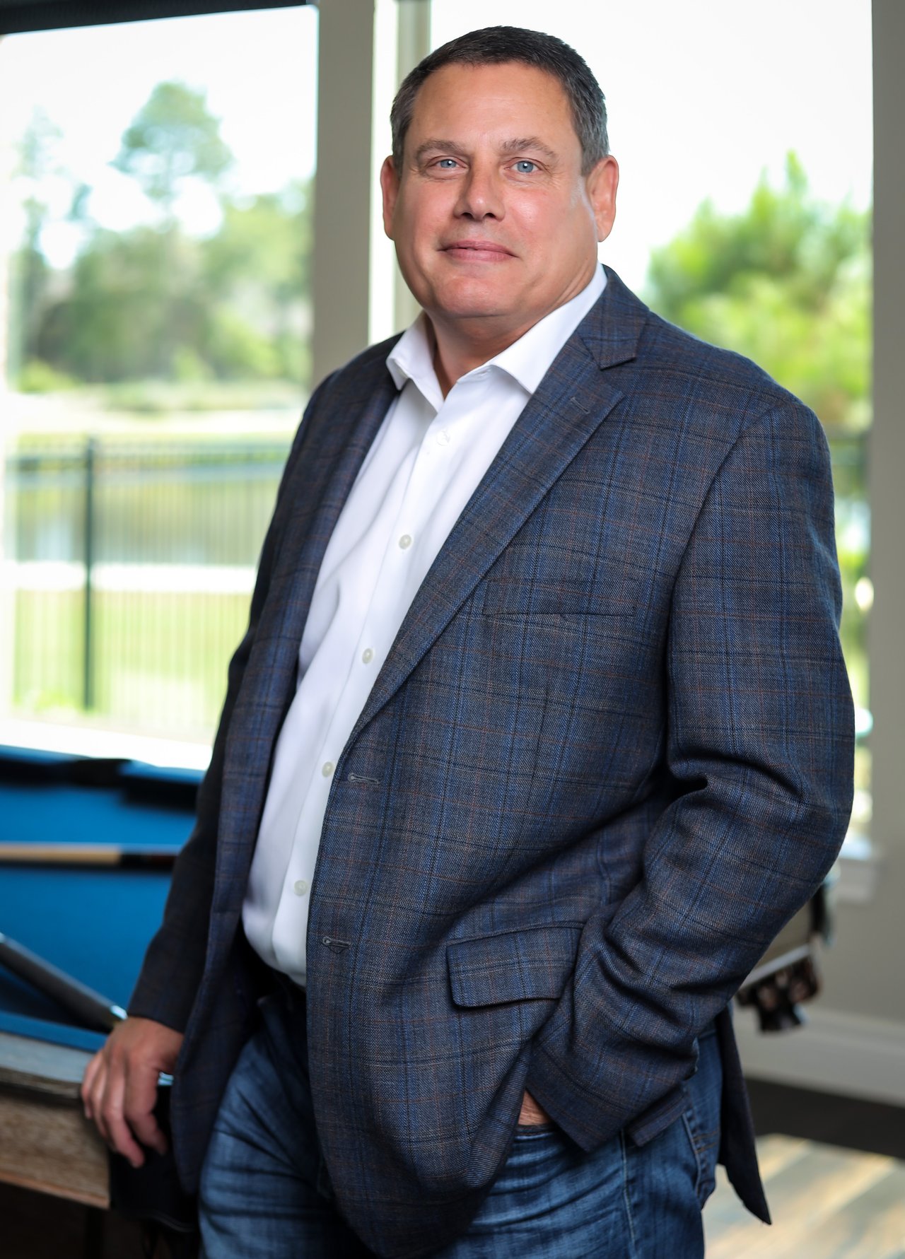 Keith Rodgers, real estate agent in Spring, TX, standing indoors by a large window in a navy blazer.