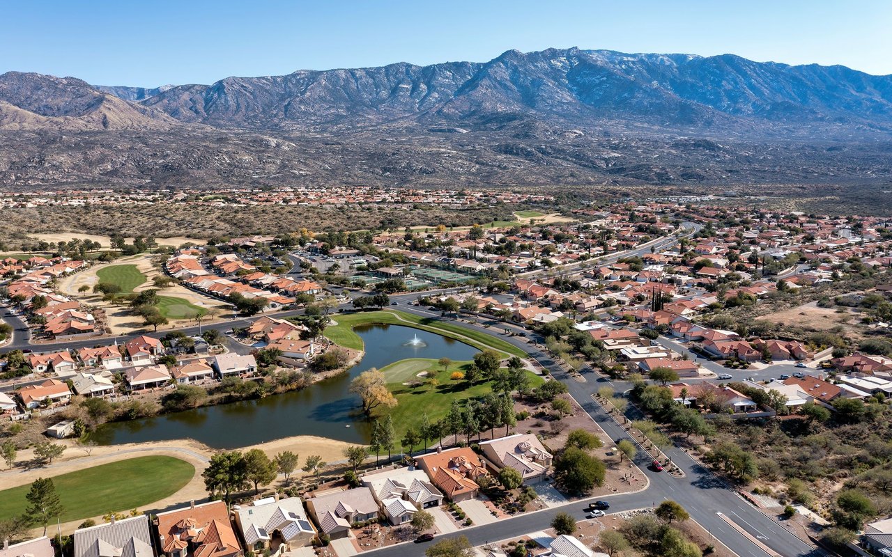Aerial neighborhood with a golf course pond and rugged mountains in the distance.