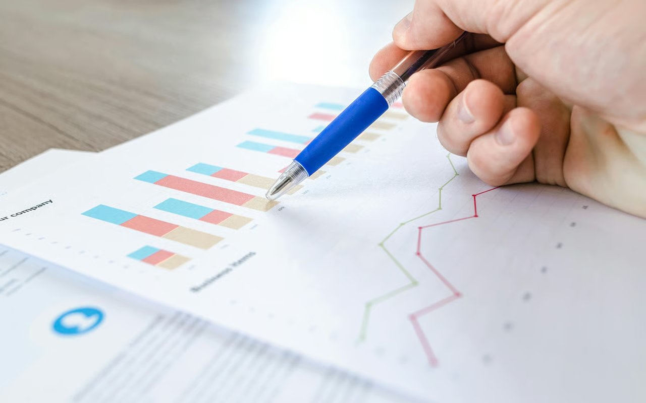 A hand points with a blue pen to bar and line charts on a financial report.