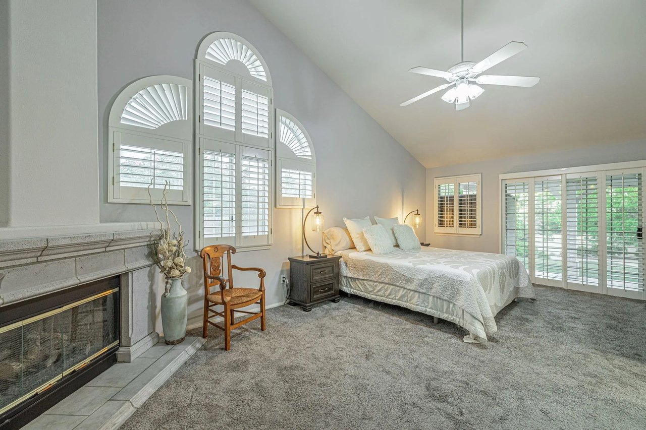 Staged bedroom with a stone fireplace, arched shuttered windows, and glass doors to the garden.