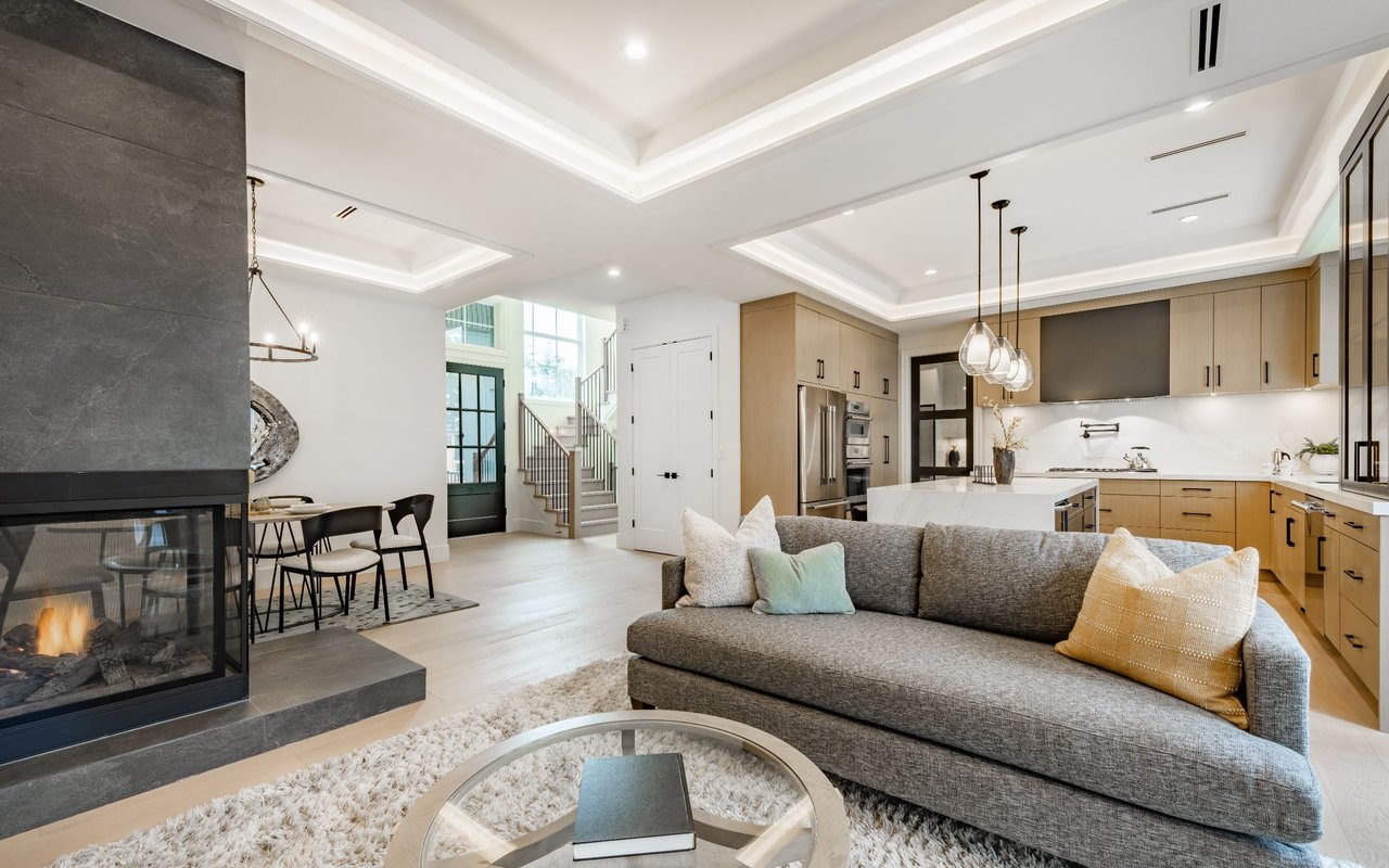 Open-plan living room with gray sectional, dark stone fireplace, and light wood kitchen cabinetry.