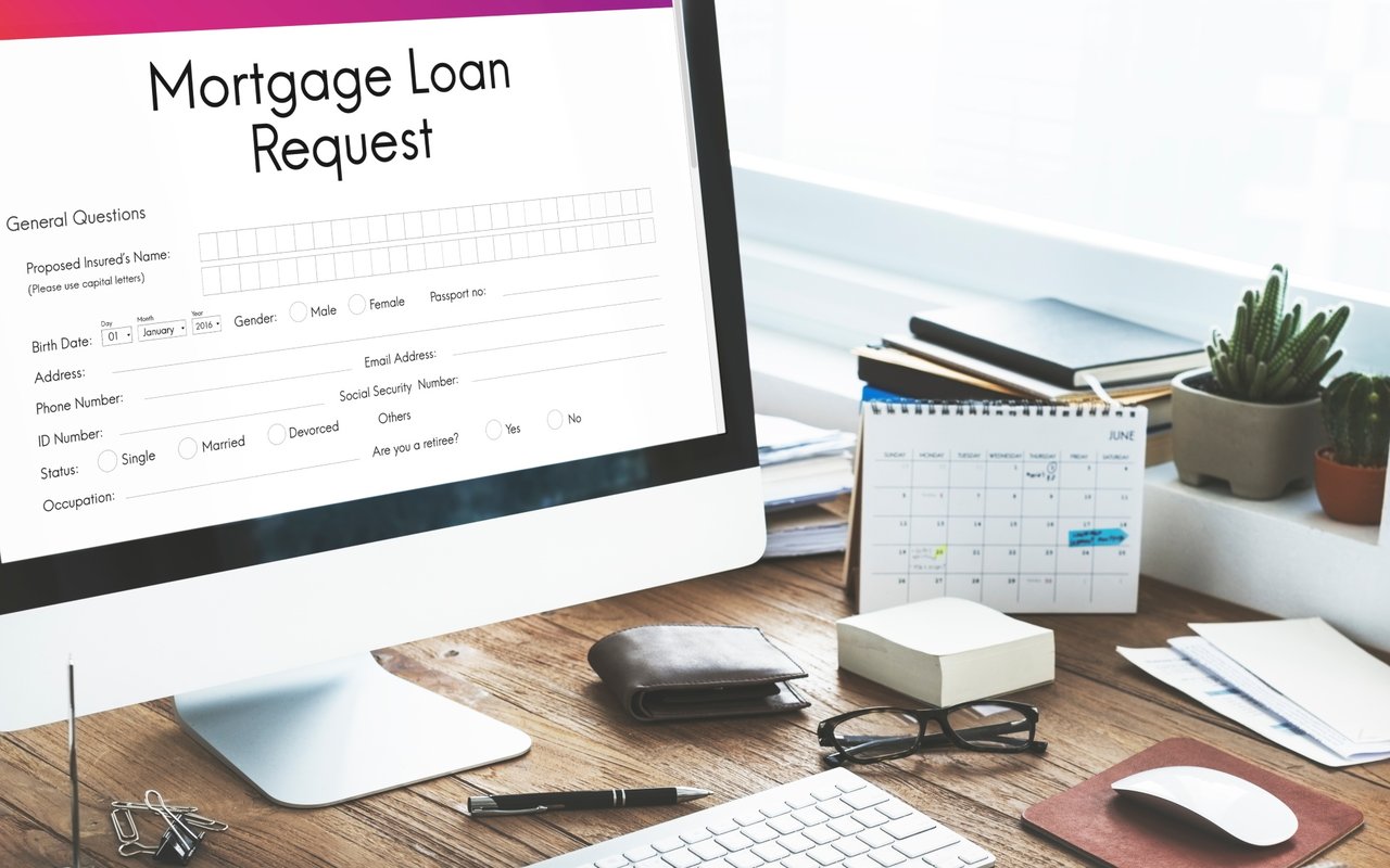 Mortgage loan request form on a desktop monitor beside a calendar and small potted cacti.