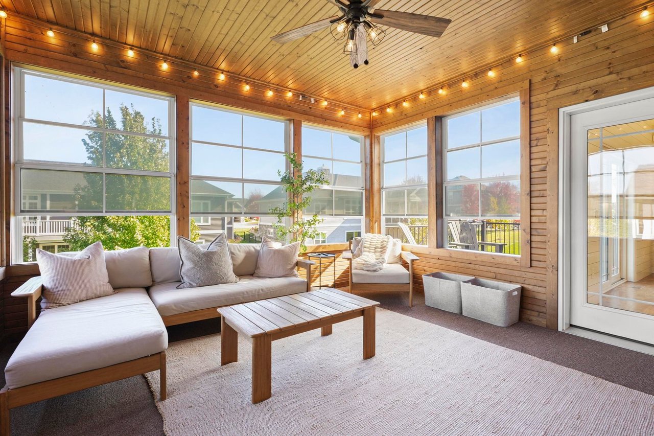 Wood-paneled sunroom with large windows, a cushioned sectional, coffee table, ceiling fan, and views of neighboring homes.