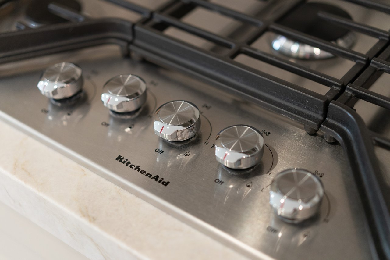KitchenAid gas cooktop with five metal knobs and black burner grates.