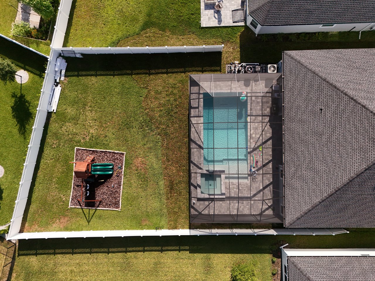 Aerial view of a fenced backyard with a screened pool and small playset.