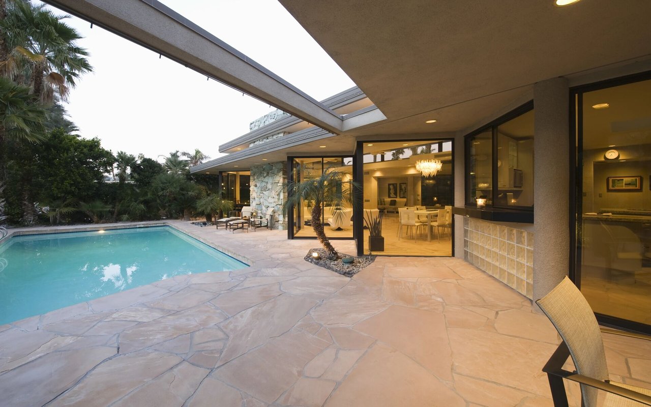Modern home patio with a swimming pool, stone paving and expansive glass doors.