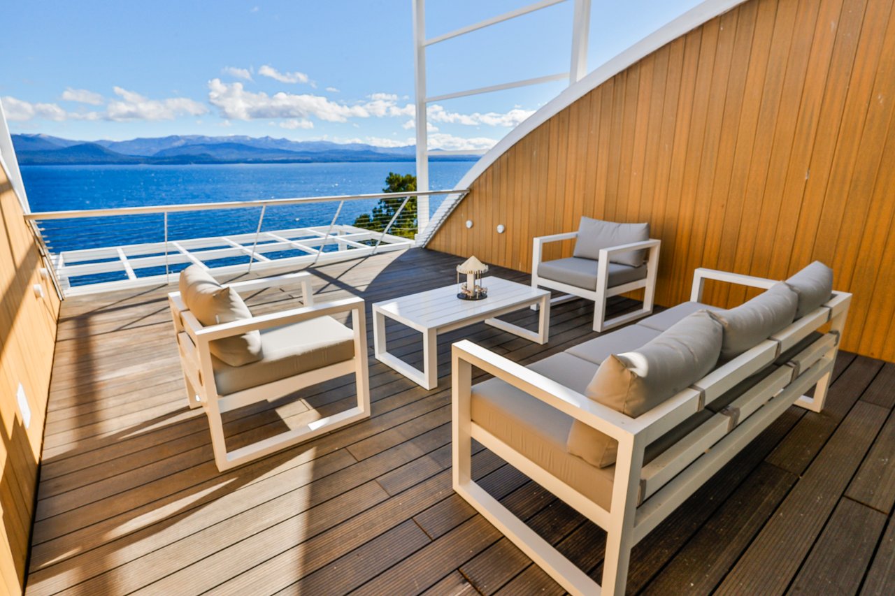 Furnished wooden terrace overlooking a blue lake and distant mountains.