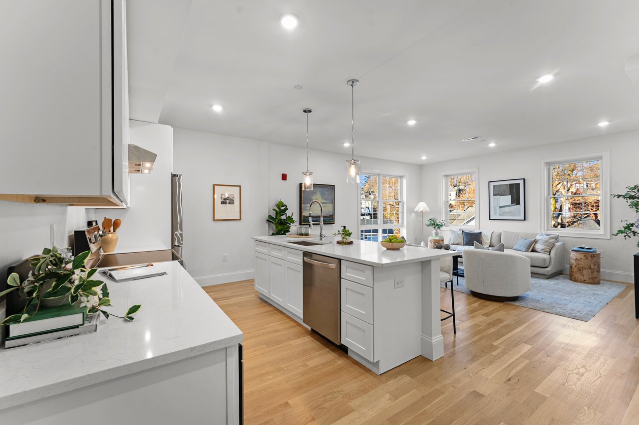 Open-plan kitchen with a large white island beside a living area with autumn views.