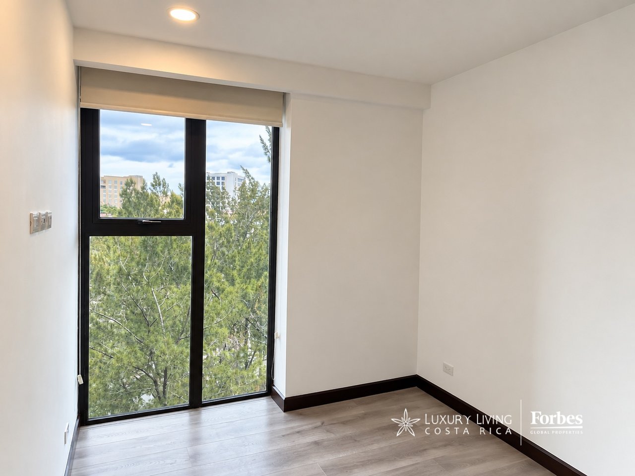 Empty apartment room with wood-look flooring and a large window overlooking trees.