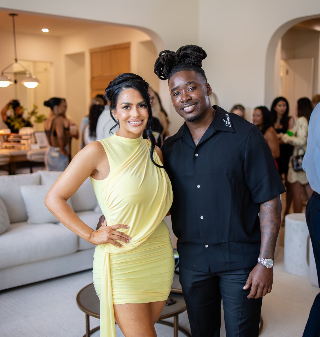 A woman in a pale yellow dress and a man in black pose together at an indoor event.