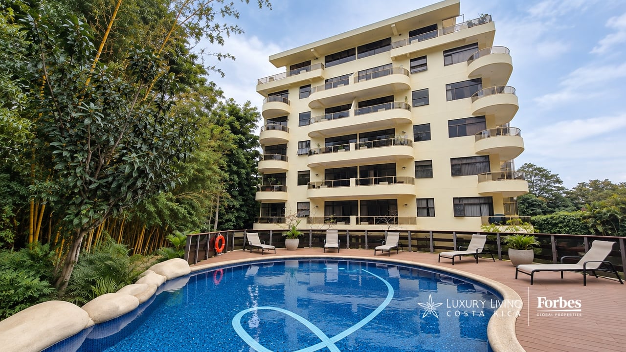 Apartment building with rounded balconies behind a landscaped swimming pool.